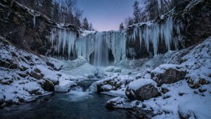 冬日星空下，冰柱与积雪点缀的壮丽瀑布。