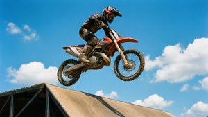 一辆泥地摩托车从斜坡上腾空起飞，背景是清澈蓝天。
