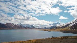 山间湖泊，远处是雪山和多云的天空。