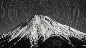 一张长时间曝光的黑白照片，星轨环绕着积雪的山峰。