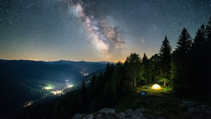 从山脊俯瞰星空夜景，营地微光闪烁。