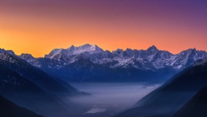 令人叹为观止的超广角视角，展现日出时分积雪山峰与雾气弥漫山谷的景象。
